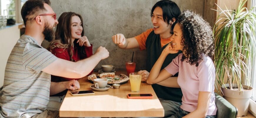 Four,Cheerful,Friends,Sitting,Around,A,Restaurant,Table,,Sharing,Delicious